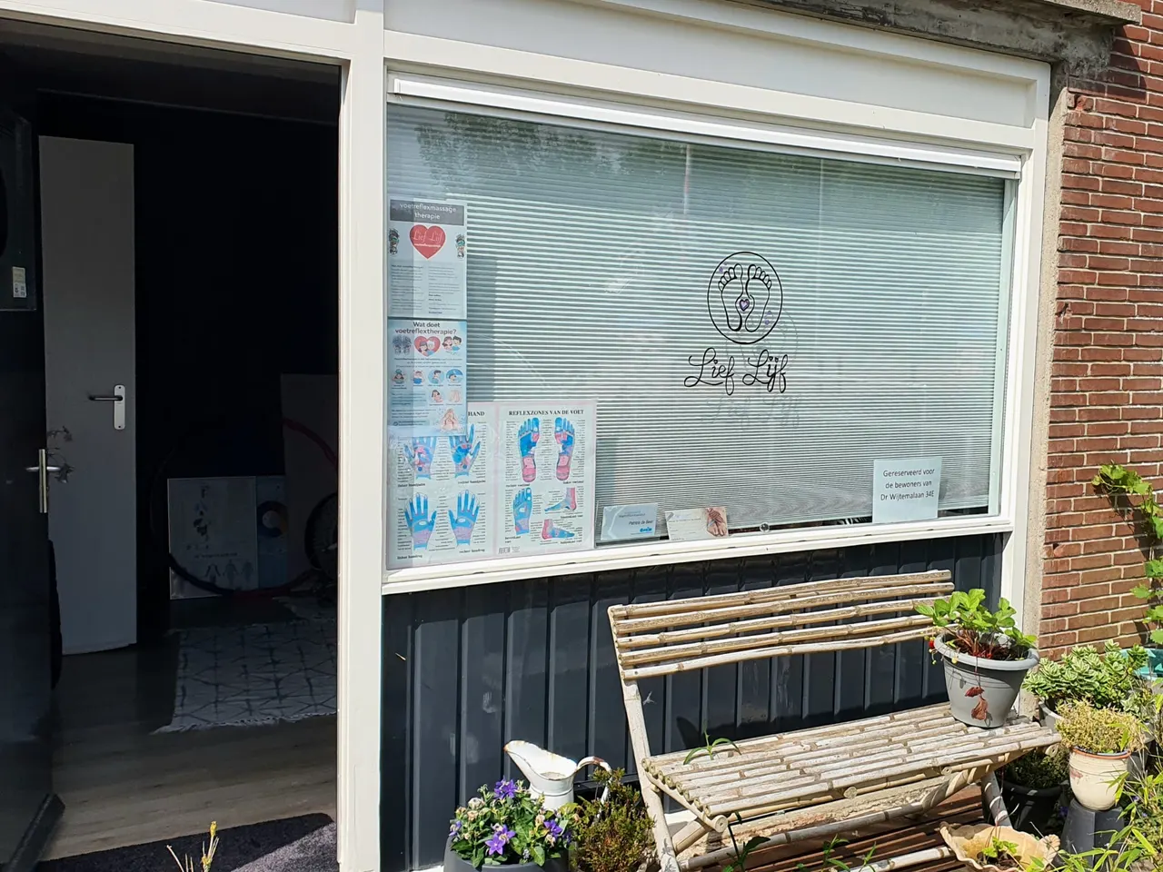 De praktijk van Lief Lijf aan de Dr. Wijtemalaan in Westwoud, met het logo op de ruit en een bankje met planten bij de deur.